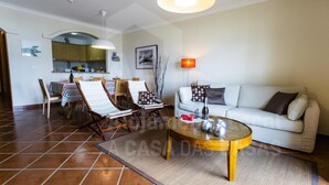A living room with a sofa, a coffee table, and a dining area with chairs and a table. - Kiko s House by Acasadascasas (Mafra)