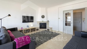 A living room with a TV, fireplace, and a door leading to another room. - Ocean Apartment by Acasadascasas (Mafra)