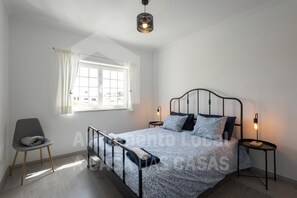 A bedroom with a bed, a chair, a window, and a hanging light fixture. - Ocean Apartment by Acasadascasas (Mafra)