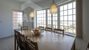 A dining area with a large table, chairs, and hanging pendant lights. - Ocean Apartment by Acasadascasas (Mafra)