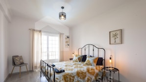 A bedroom with a bed, a chair, a window, and a door. - Ocean Apartment by Acasadascasas (Mafra)
