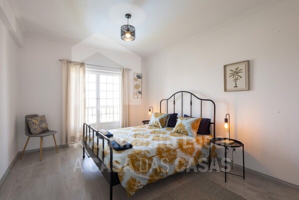 A bedroom with a bed, a chair, a window, and a door. - Ocean Apartment by Acasadascasas (Mafra)