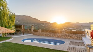 Ein Poolbereich mit Steinmauer, Holzterrasse und einer Pergola mit Tisch und Stühlen.