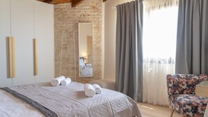 Ein Schlafzimmer mit einem großen Bett, einem Holzstuhl, einem Spiegel und einer Steinwand.