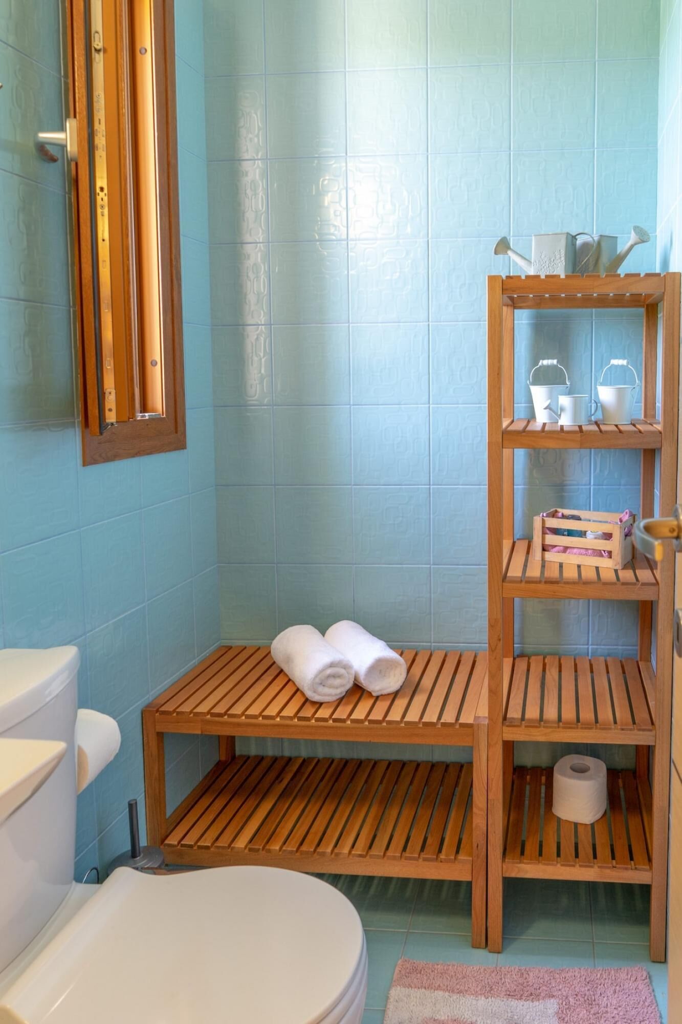 Een badkamer met een houten bankje, een toilet en een plank met toiletartikelen.