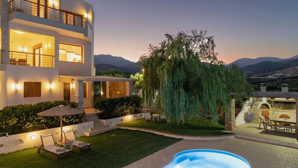 Ein modernes, zweistöckiges Haus mit Swimmingpool, Sitzgelegenheiten im Freien und einem großen Baum.