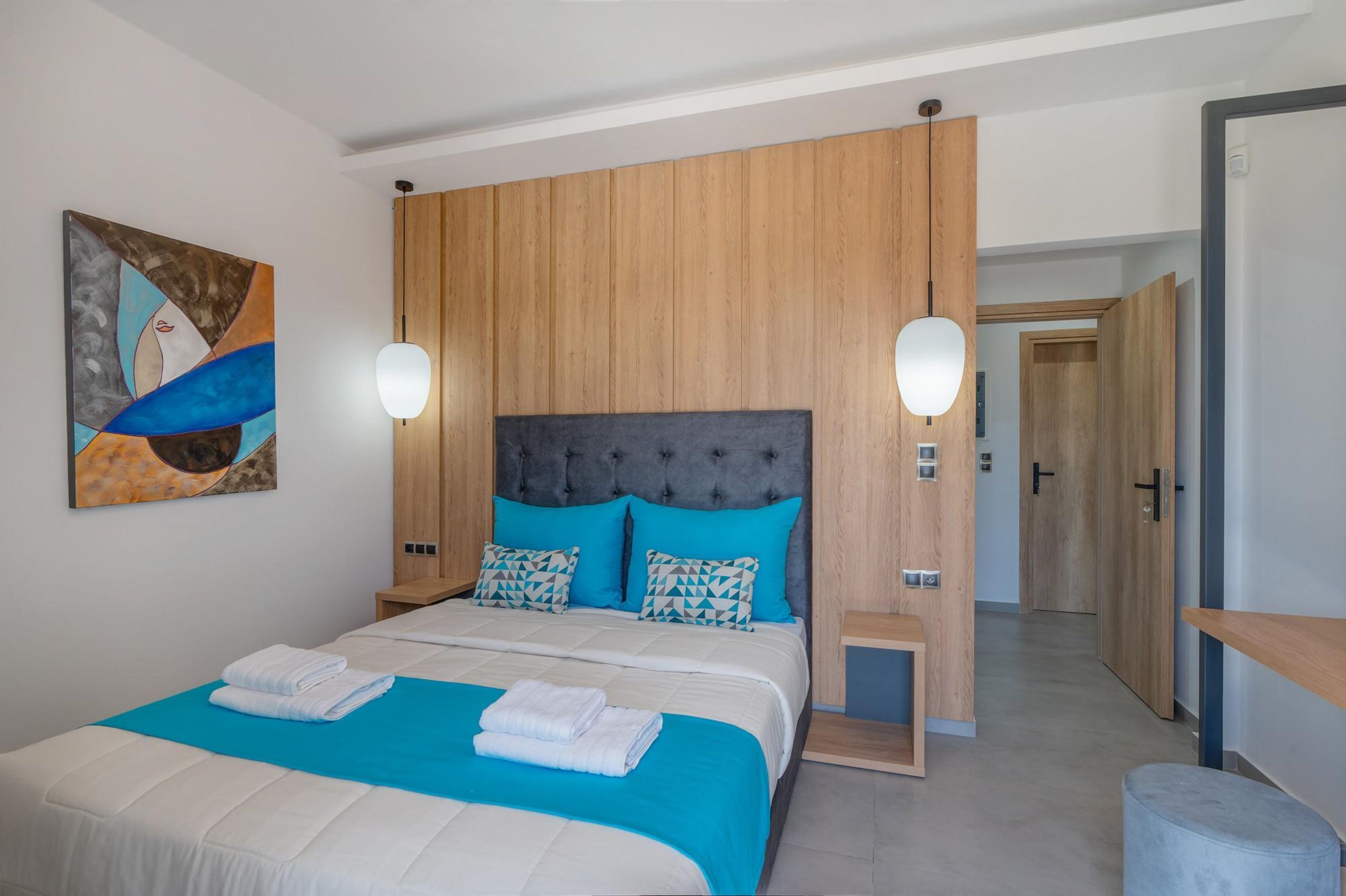 A modern hotel room with a large bed, wooden paneling, and a painting on the wall.