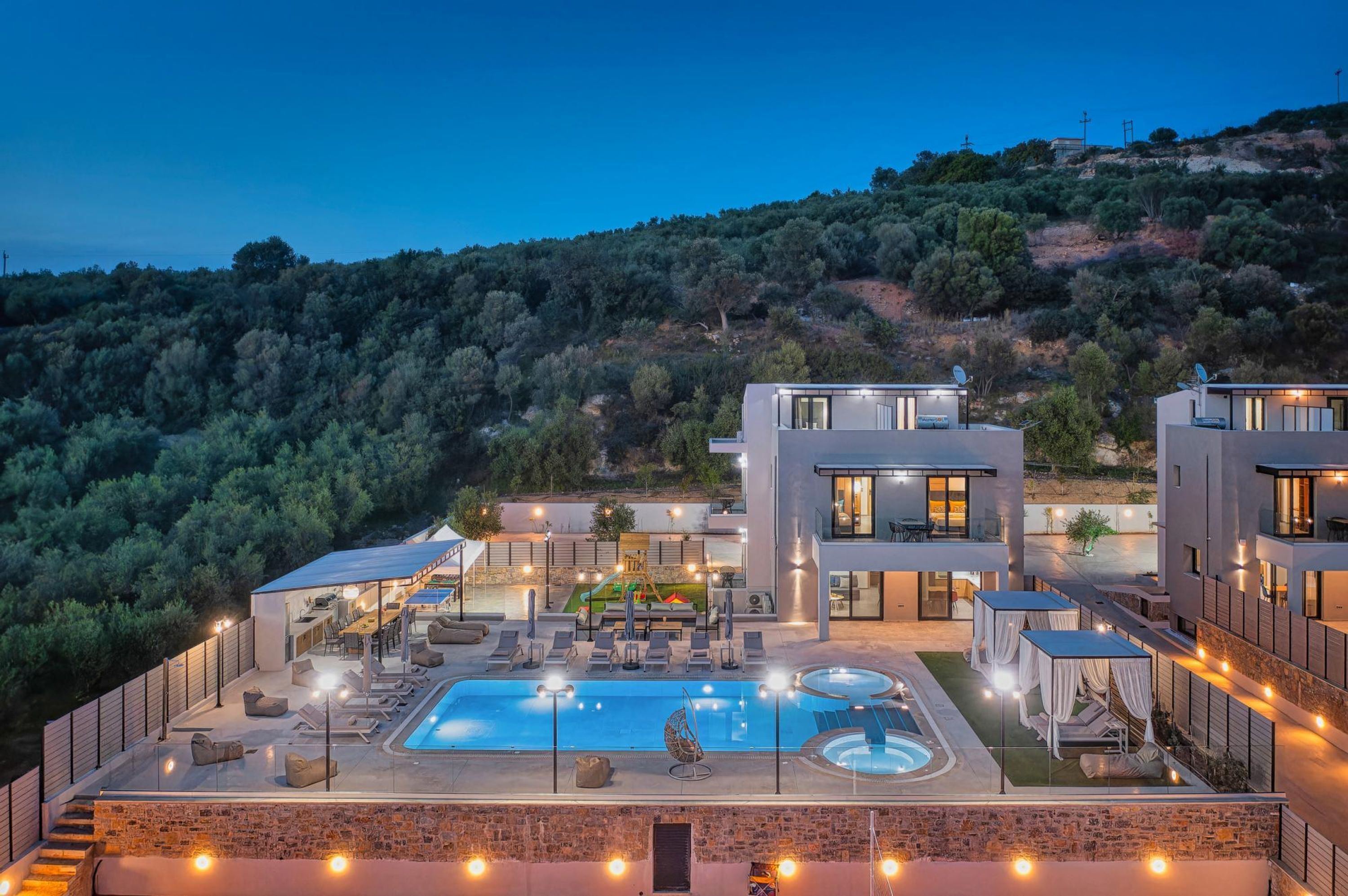A modern villa with a swimming pool, outdoor seating, and a view of a hilly landscape.