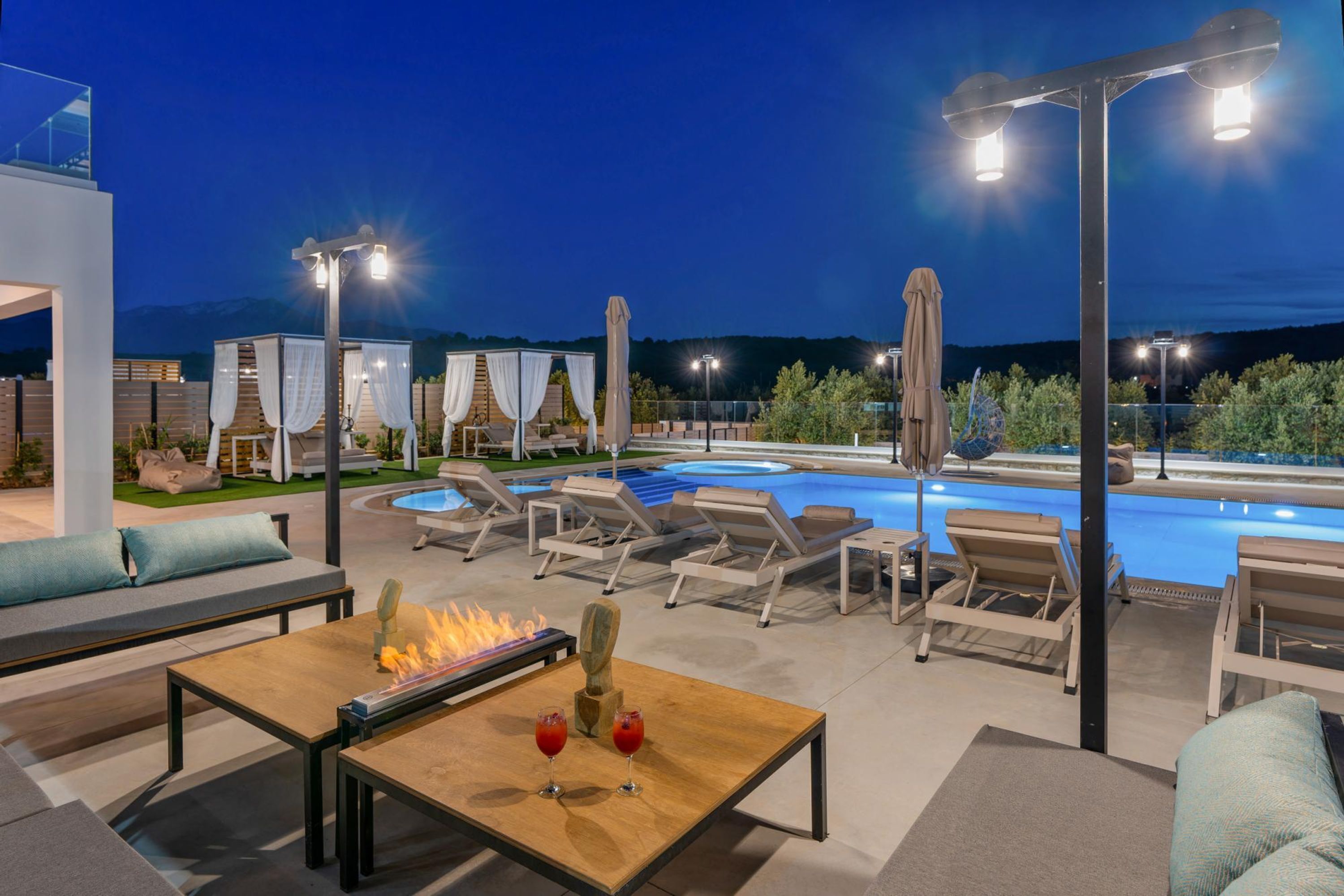 An outdoor pool area with lounge chairs, a fire feature, and ambient lighting.