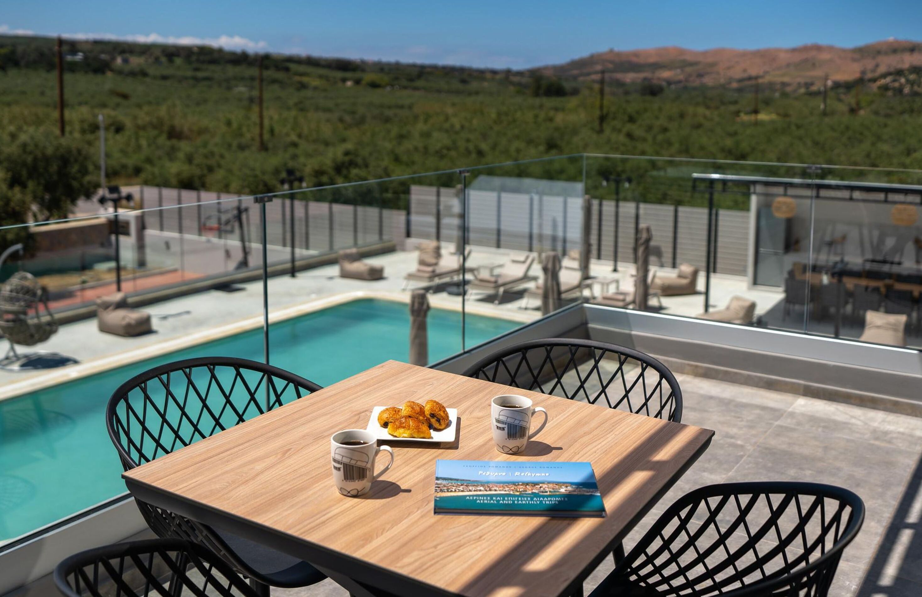 A poolside table with a book, two cups, and a plate of pastries.