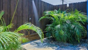 Ein Holzzaun mit Wasserspiel, Palmen und einem Betonweg.
