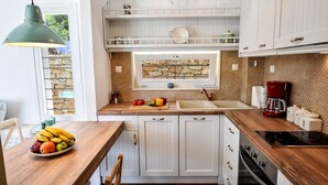 A kitchen with white cabinets, a wooden countertop, a stone backsplash, and a window with a stone wall view. - Apeiron II Villa - Sunny Modern Pool - Walk to Gaios (Paxos)
