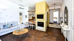 A modern living room with a sofa, coffee table, and fireplace. A kitchen is visible in the background. - Apeiron II Villa - Sunny Modern Pool - Walk to Gaios (Paxos)