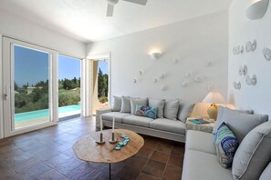 A modern living room with a sofa, coffee table, and decorative wall lights. - Apeiron II Villa - Sunny Modern Pool - Walk to Gaios (Paxos)