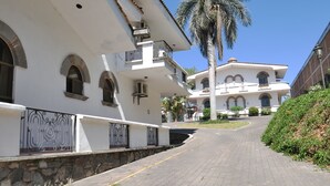A multi-story building with arched windows and balconies, a paved pathway leading to it, and a palm tree in the foreground. - Hotel Hacienda las Higueras  (Tepic)