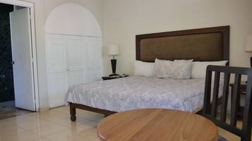 A hotel room with a bed, a bedside table with a lamp, a chair, and a round table.
