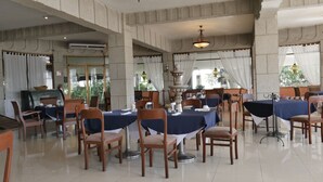 A spacious dining area with multiple tables and chairs, a central fountain, and large windows with curtains. - Hotel Hacienda las Higueras  (Tepic)