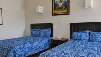 A hotel room with two beds, each with blue patterned bedding, a small bedside table with a phone, and a painting on the wall.