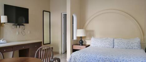 A hotel room with a bed, a desk with a chair, a television, and a mirror.