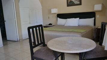 A hotel room with a bed, a round table, two chairs, a door, and a painting on the wall.