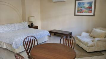 A bedroom with a bed, bedside table, lamp, chair, sofa, and a small table.
