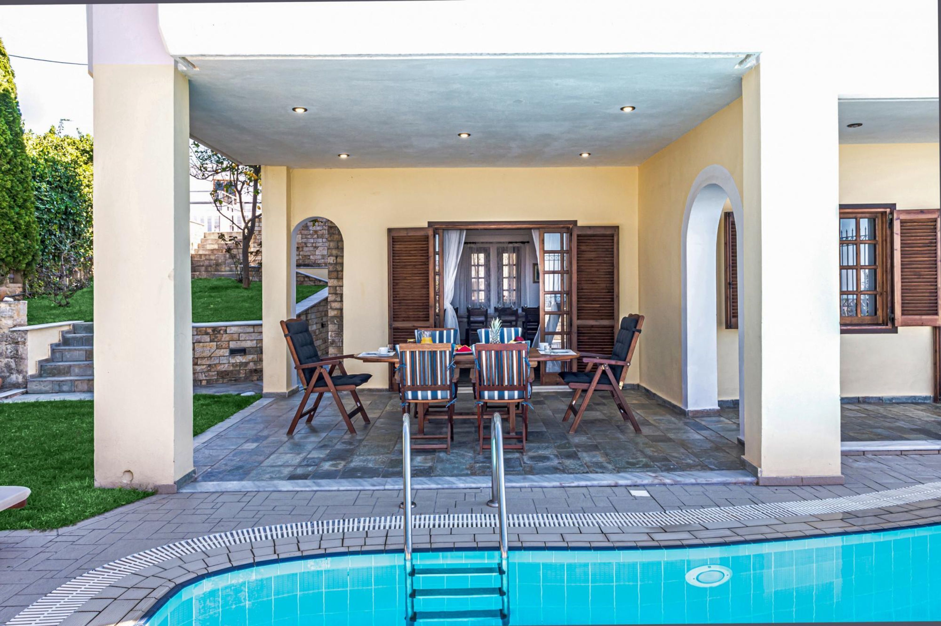 A covered outdoor patio with a pool, stone flooring, and a dining area with tables and chairs.
