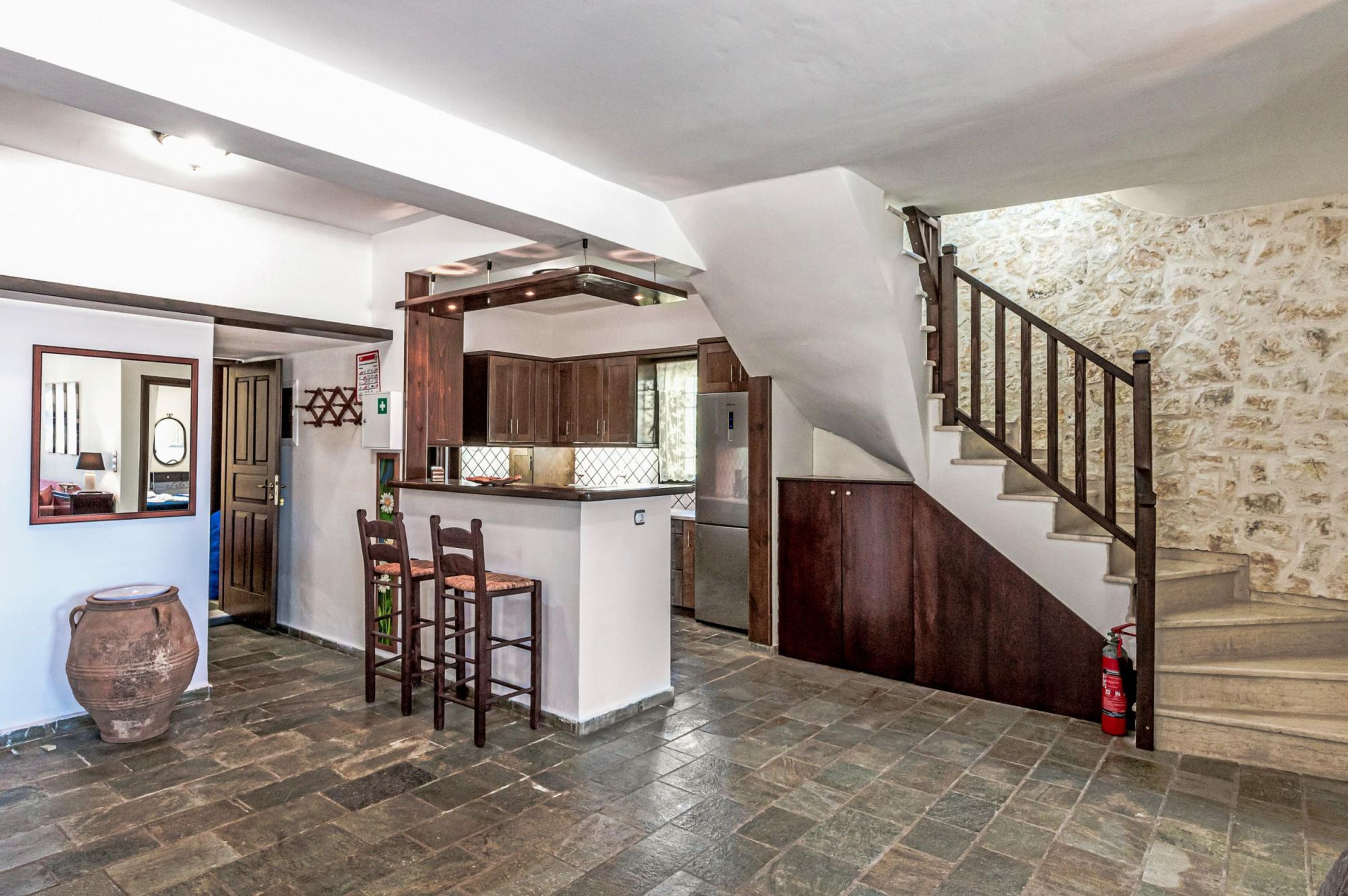 A spacious kitchen with a central island, wooden bar stools, and a stone staircase leading to an upper level.