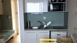 A compact kitchen with a sink, microwave, and coffee maker. There's a small dining area with a table and chairs. - Face mer Plage à 2m Studio 4 Personnes (Sète)