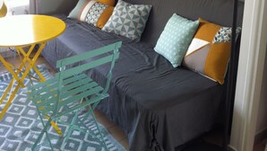 A compact room with a sofa bed, a small table, and a floor lamp. - Face mer Plage à 2m Studio 4 Personnes (Sète)