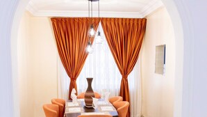A dining area with a table set for six, surrounded by orange chairs, under a white archway with orange curtains. - Family sized house with a summer hut for outdoor sitting (Tema)