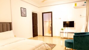 A hotel room with a bed, a desk with a flat-screen TV, a teal chair, and a small plant. - Family sized house with a summer hut for outdoor sitting (Tema)