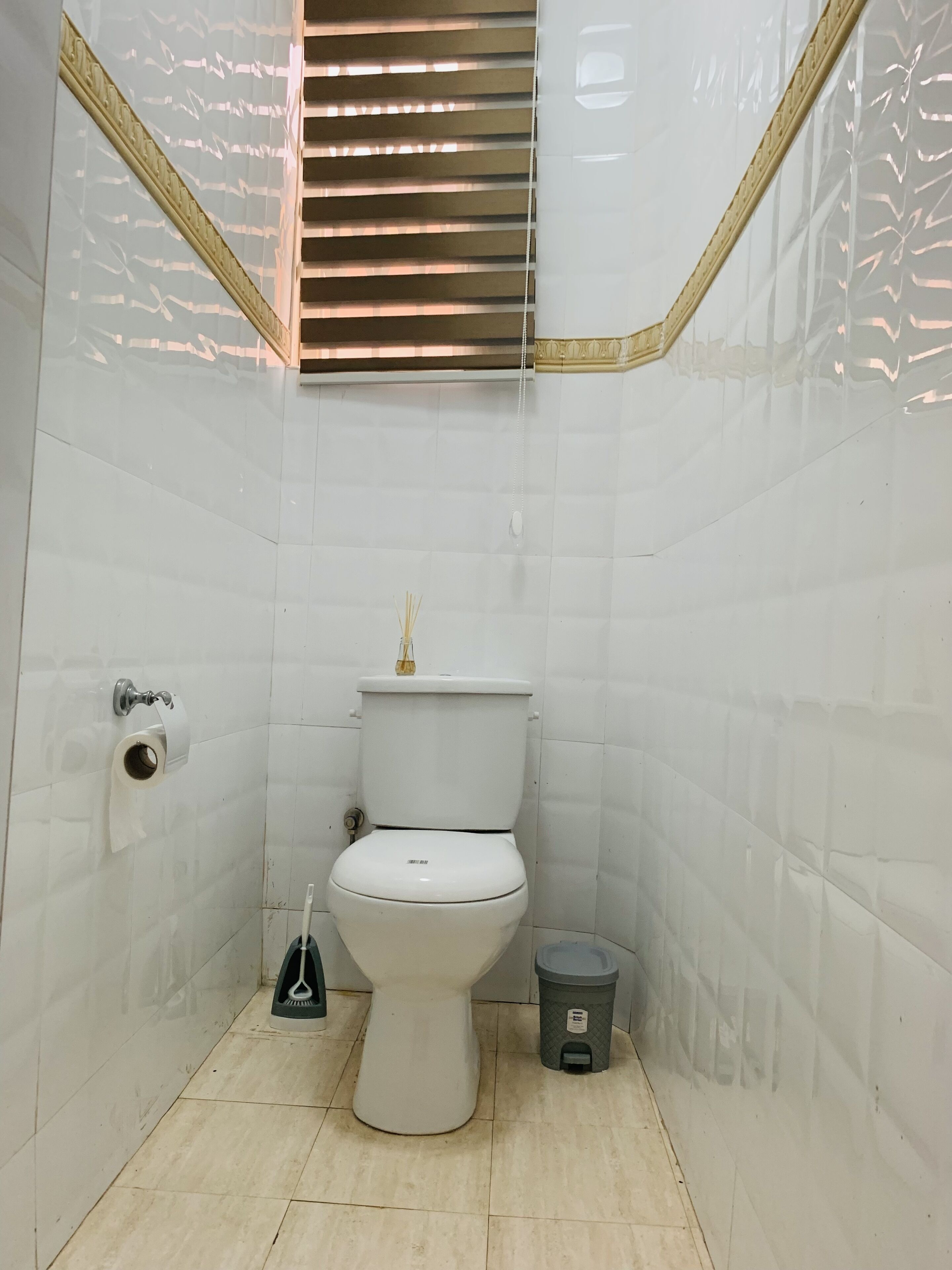 Un baño pequeño y limpio con inodoro, un cesto de basura y un dispensador de papel higiénico.