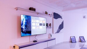 A modern living room with a large flat-screen TV mounted on the wall, a minimalist console table, and a few decorative items. - Family sized house with a summer hut for outdoor sitting (Tema)