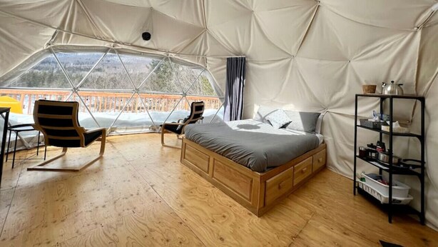 A spacious tented room with a wooden bed, a chair, and a shelf. - Dome # 1 with view to the mountains (Saint-Gabriel-de-Valcartier)