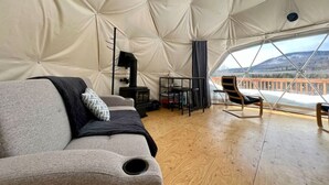 A cozy interior with a sofa, a small table, and a chair, and a view of a snowy landscape through large windows. - Dome # 1 with view to the mountains (Saint-Gabriel-de-Valcartier)