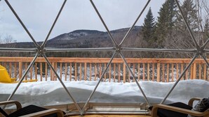 A deck with two chairs and a wooden railing, overlooking a snowy landscape with a mountain in the background. - Dome # 1 with view to the mountains (Saint-Gabriel-de-Valcartier)