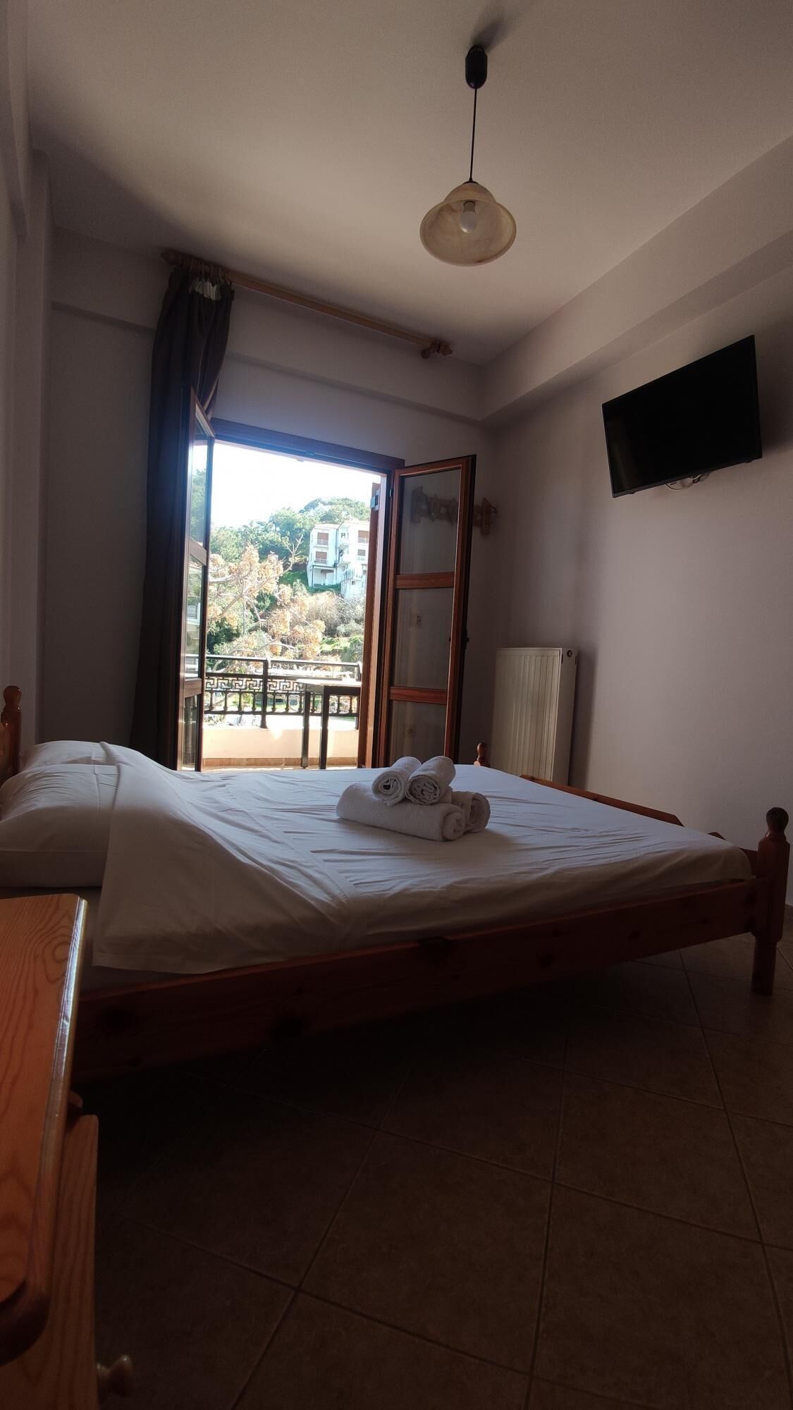 A bedroom with a bed, a TV mounted on the wall, and a view of a balcony with a railing.