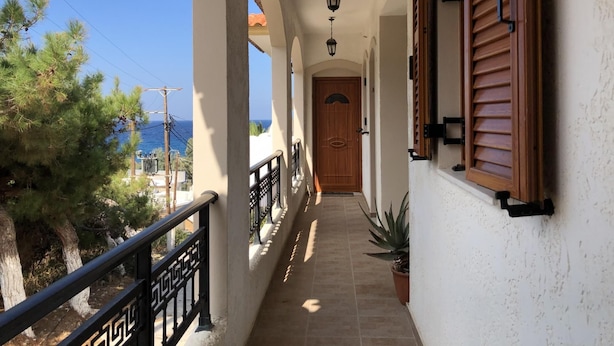 A corridor with a wooden door, a potted plant, and a railing. - Nikos Apartments A2 in Gialiskari (Ikaria)