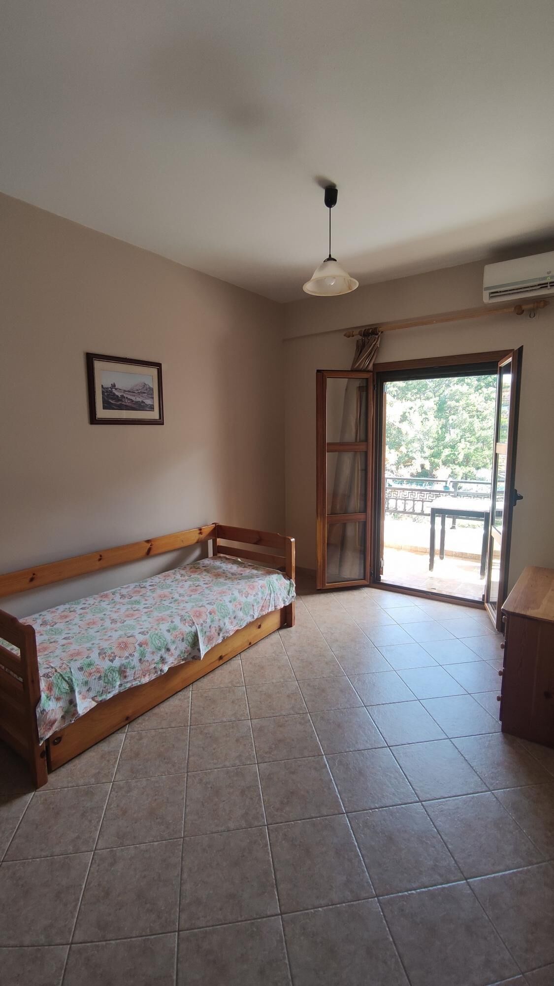 Una habitación con sofá cama de madera, ventilador de techo, un cuadro enmarcado en la pared y puerta corrediza de vidrio que da a un espacio al aire libre.