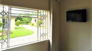A room with a large window, a flat-screen TV mounted on the wall, and a view of a garden and building outside.