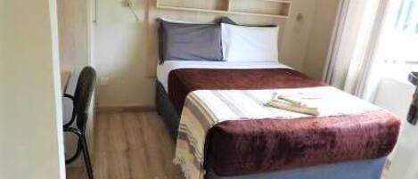 A small, neatly arranged bedroom with a single bed, a chair, and a bedside table.