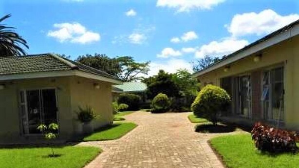 A pathway leading to a building with a tiled roof, surrounded by well-maintained grass and small plants.