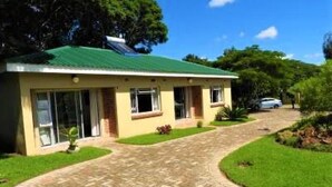 A single-story house with a green roof, a paved driveway, and a well-maintained lawn.