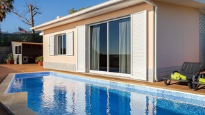 Ett modernt hus med en swimmingpool, stora skjutbara glasdörrar och en uteplats med utemöbler.