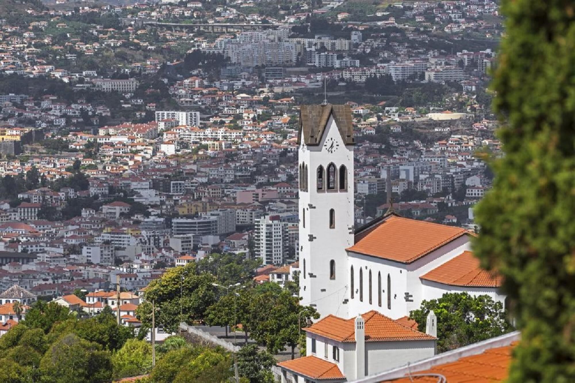 A white church with a clock tower, surrounded by a densely packed urban area with red-tiled roofs.
