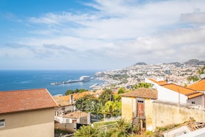 A coastal cityscape with terracotta-roofed buildings, a marina, and a distant hill. - Uptown Sea View by Homie (Funchal)