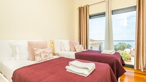 Une chambre d’hôtel avec deux lits, une grande fenêtre donnant sur la mer et un balcon.