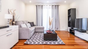 Un salon moderne avec un canapé gris, une table basse noire, un téléviseur à écran plat et un plancher en bois.