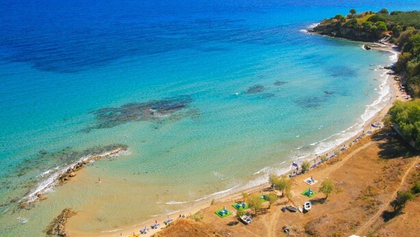A coastal beach with clear waters, a sandy shore, and a few umbrellas. - Villa Agricola With Private Swimming Pool (Zakynthos)