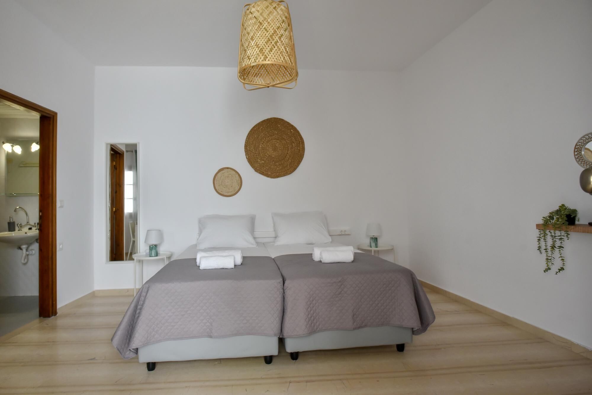 A modern bedroom with a double bed, a bedside table with a lamp, a hanging light fixture, and a wall-mounted mirror.